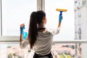 femme nettoyant une fenetre avec un vaporisateur et une racl