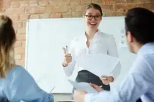 femme souriante avec lunettes pouce leve devant un tableau b